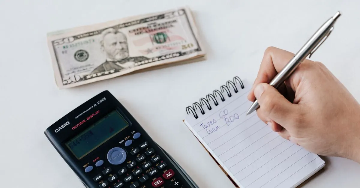 An anonymous person using a calculator and writing a budget in a notebook